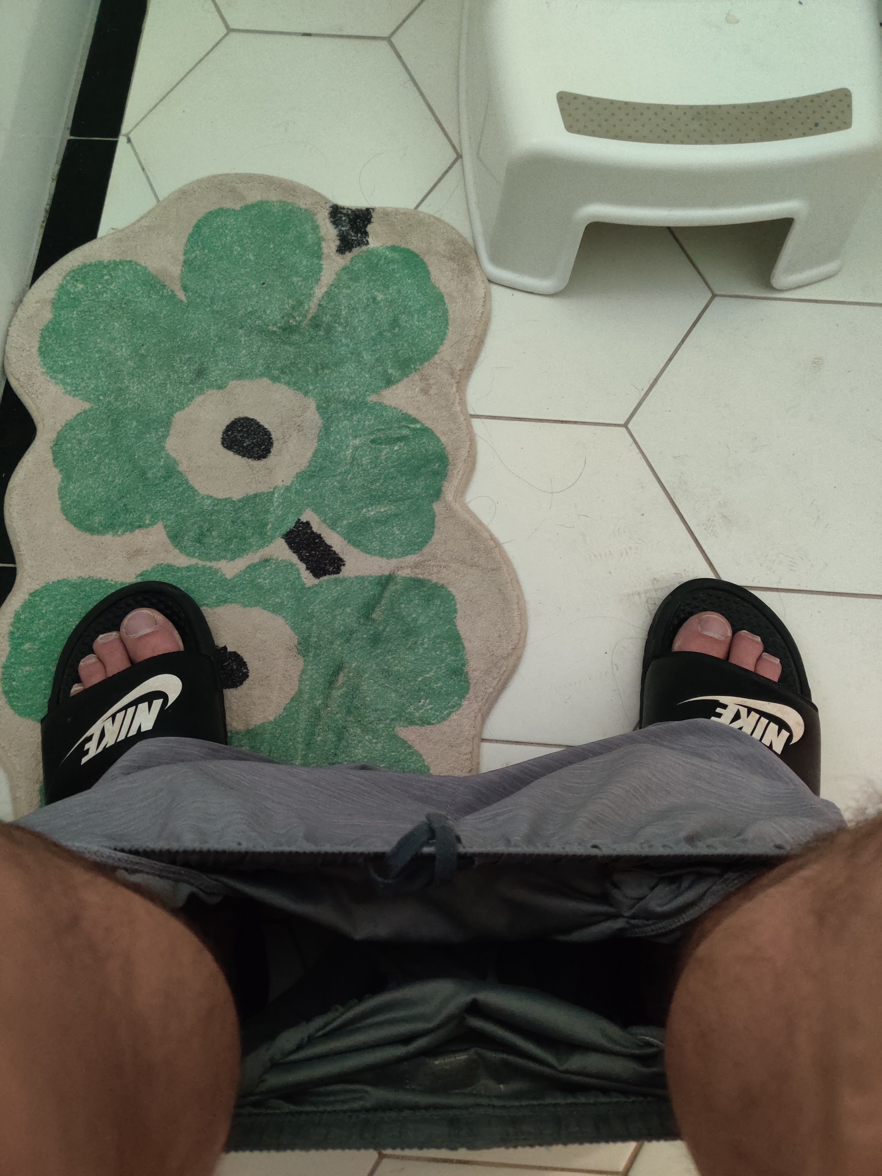 POV: you're pooping on company time, staring at your feet and a bath mat on a white, hexagonal tiled floor.